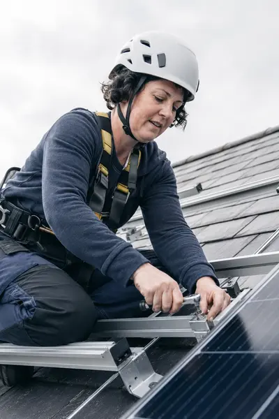 An installer kneeling on a roof bolting solar panel mounting rails into place, typical of the work SEAI registered installers in Carlow carry out